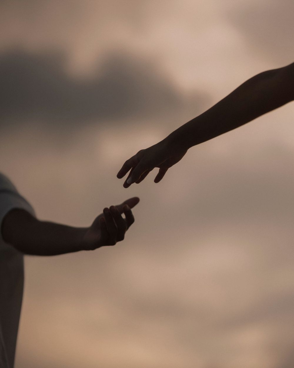 Two hands reaching toward each other, silhouetted against a soft dusk sky